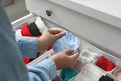 Photo of Woman putting beautiful panties into organizer with underwear in drawer, closeup