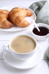 Fresh croissants, jam and coffee on white wooden table. Tasty breakfast