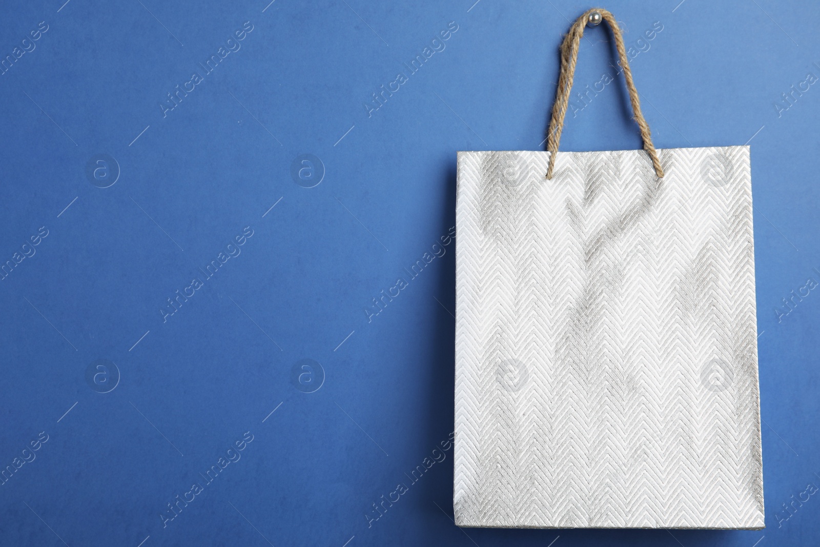 Photo of Silver shopping paper bag on blue background, space for text