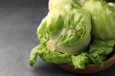 Photo of Bowl with fresh green iceberg lettuce heads and leaves on grey table, closeup. Space for text
