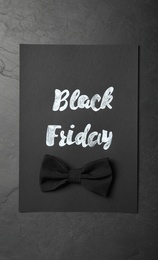 Photo of Card with phrase Black Friday and bow tie on dark background, top view