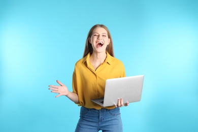 Photo of Emotional young woman with laptop celebrating victory on color background