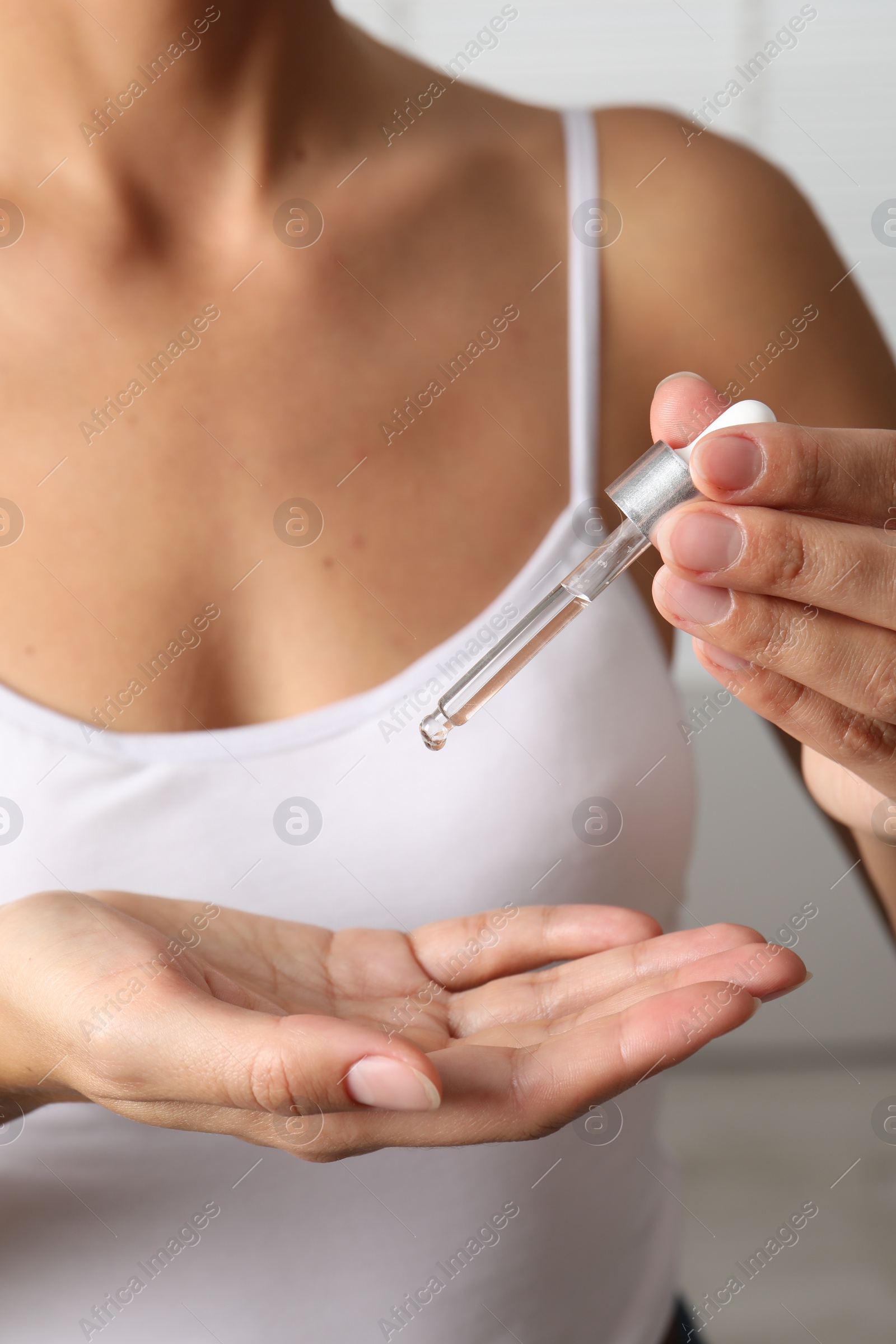 Photo of Woman applying cosmetic serum onto her hand on blurred background, closeup