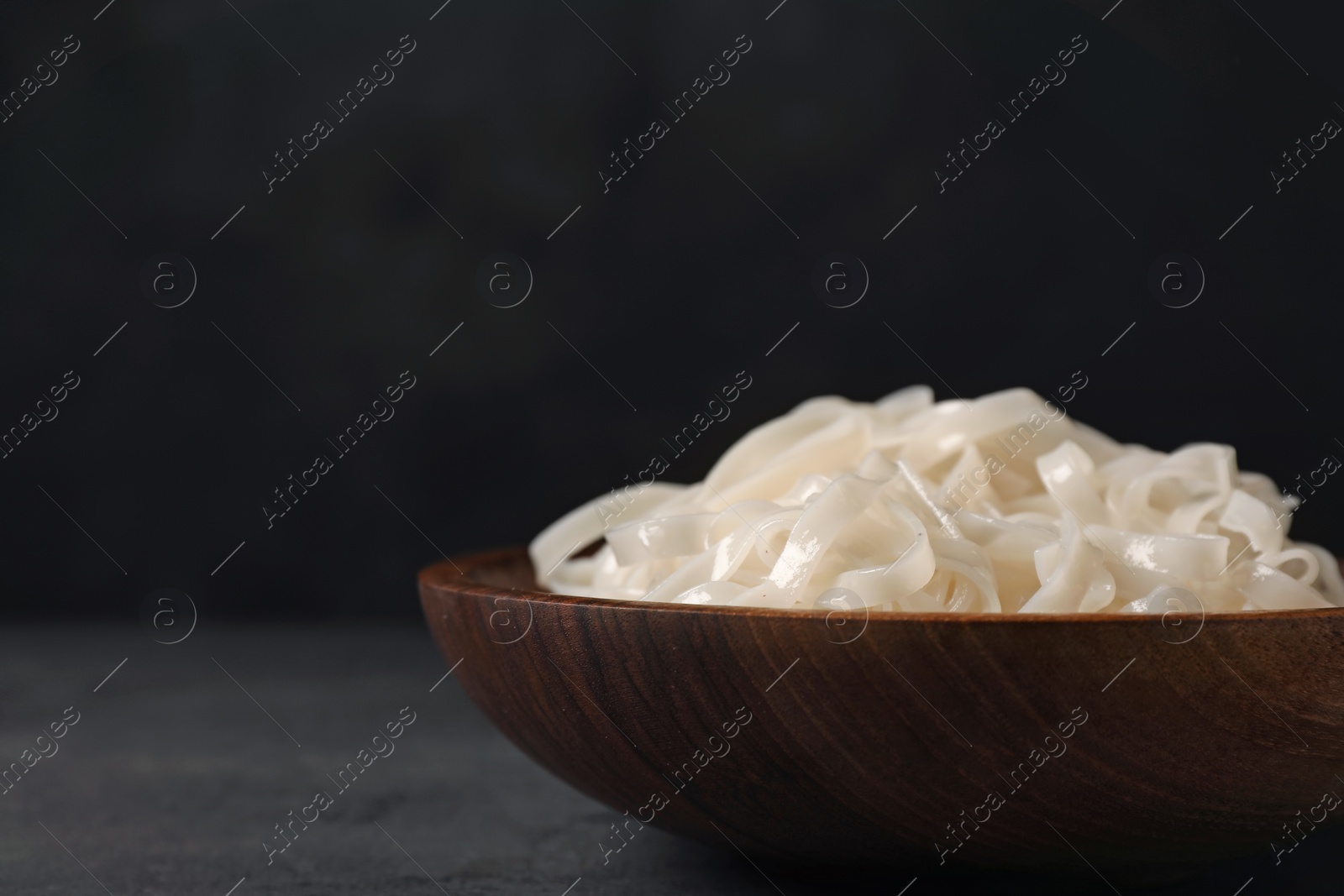 Photo of Bowl with rice noodles on table in darkness. Space for text