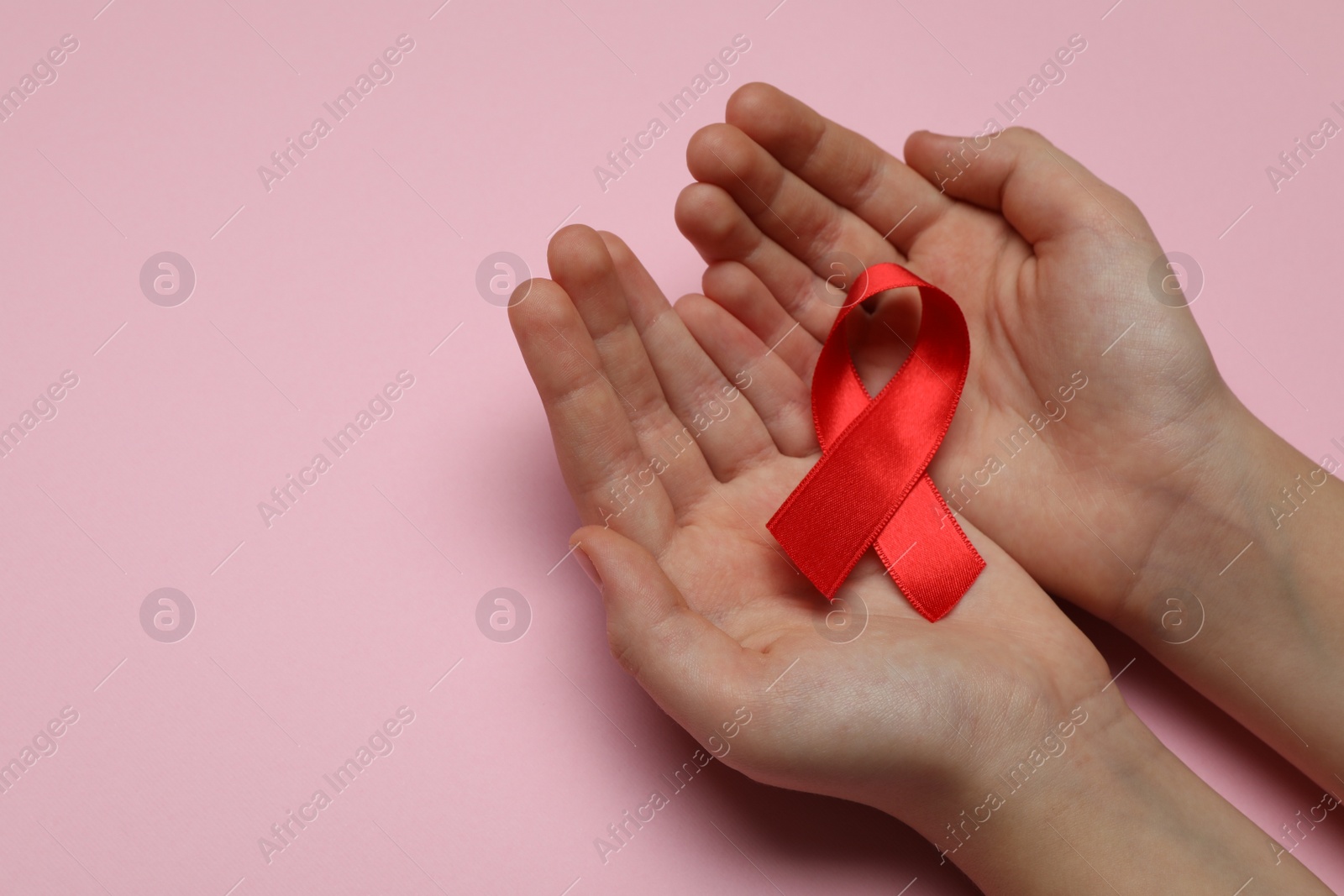 Photo of Little girl holding red ribbon on pink background, closeup with space for text. AIDS disease awareness