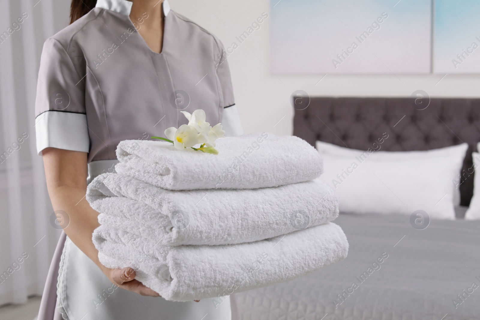 Photo of Maid holding fresh towels with flowers in hotel room, closeup