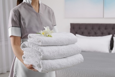 Maid holding fresh towels with flowers in hotel room, closeup