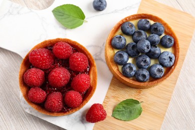 Photo of Tartlets with different fresh berries on light wooden table, top view. Delicious dessert