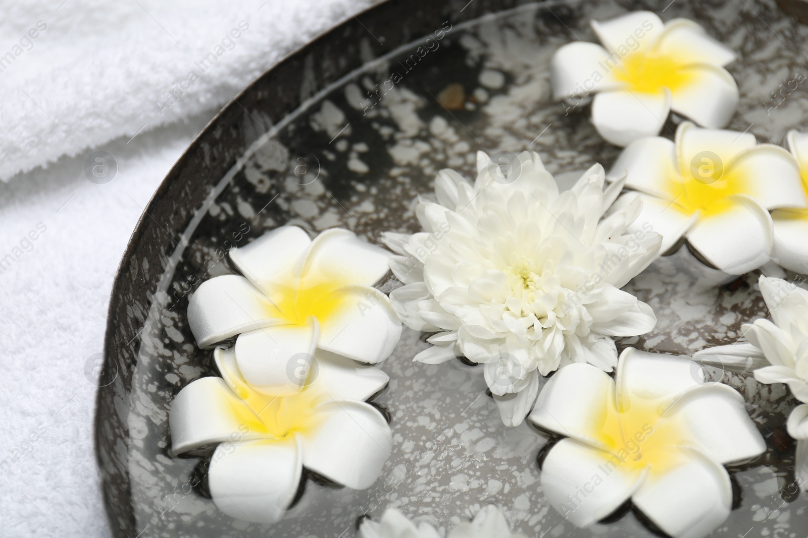 Photo of Bowl of water with flowers and towel on table, closeup. Spa treatment