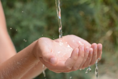 Photo of Pouring water into kid`s hands outdoors, closeup