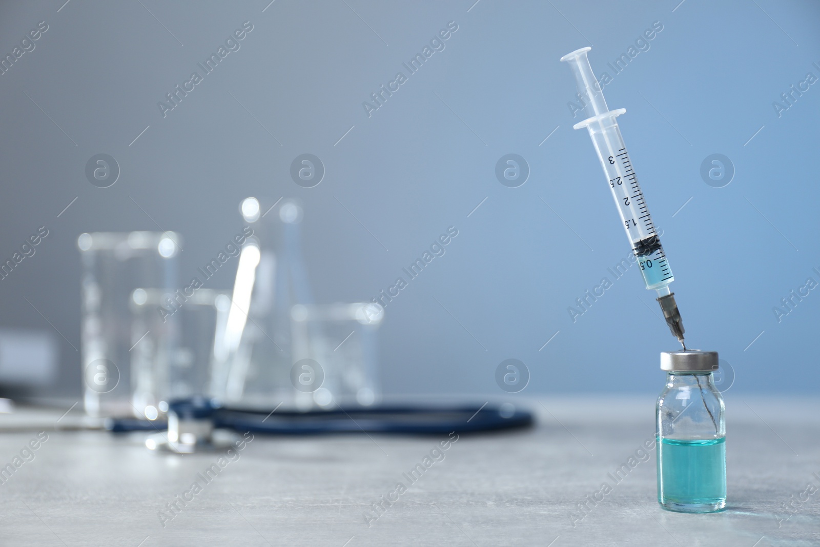 Photo of Syringe and vial on light grey table. Space for text