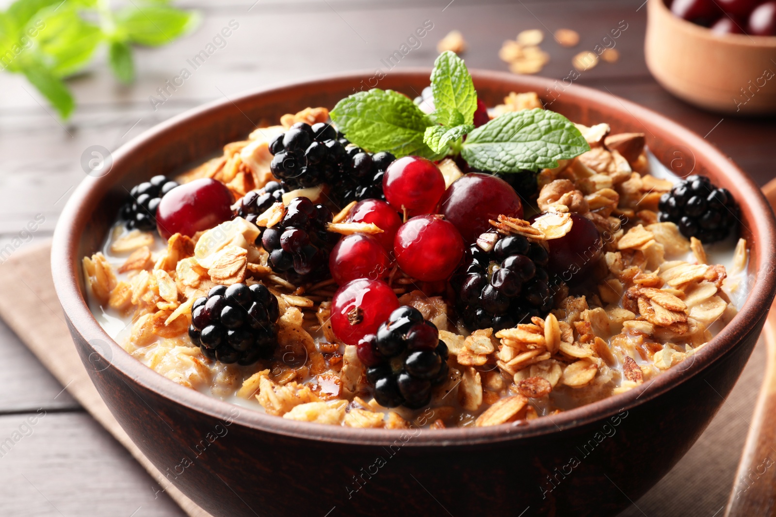 Photo of Bowl of muesli served with berries and milk on wooden table, closeup