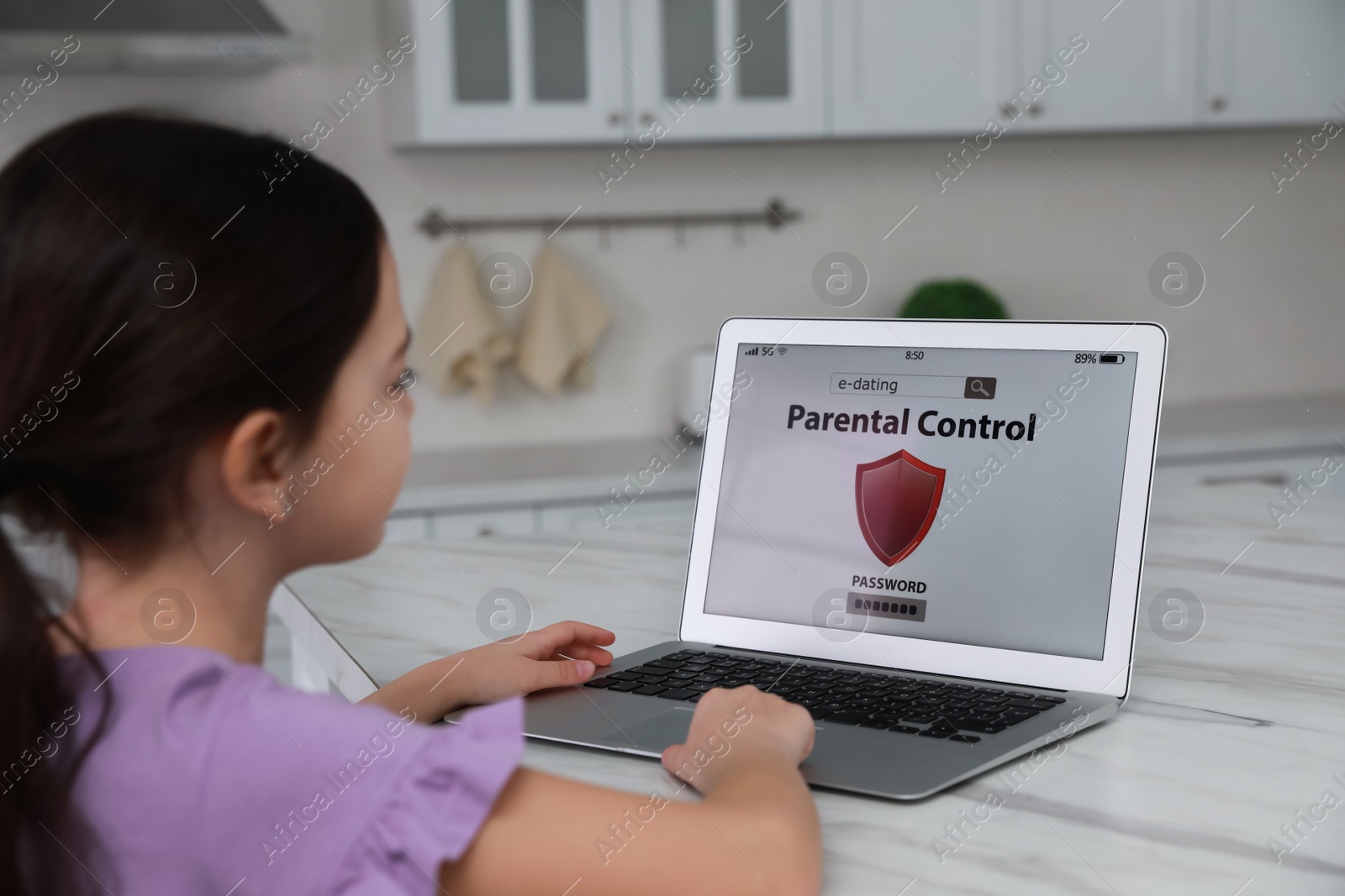 Photo of Little girl having access restriction by parental control on laptop in kitchen. Child safety