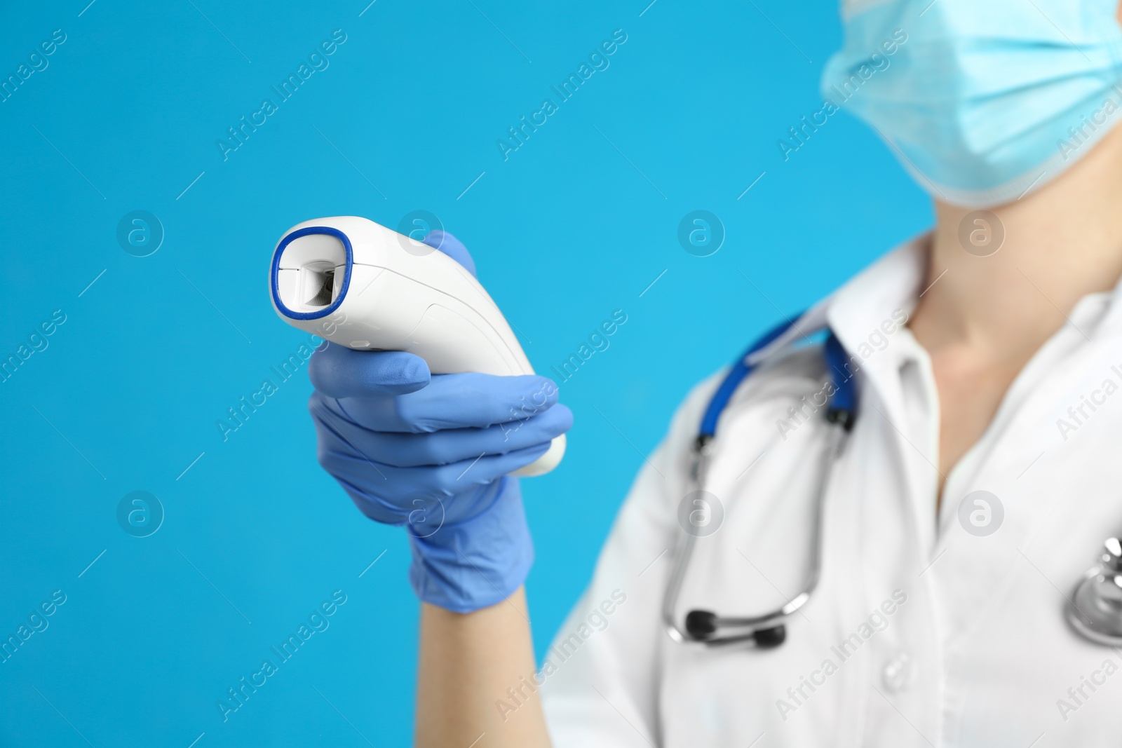 Photo of Doctor holding non contact infrared thermometer against light blue background, focus on hand. Measuring temperature