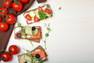 Photo of Tasty rye crispbreads with salmon, cream cheese and vegetables on white wooden table, flat lay. Space for text