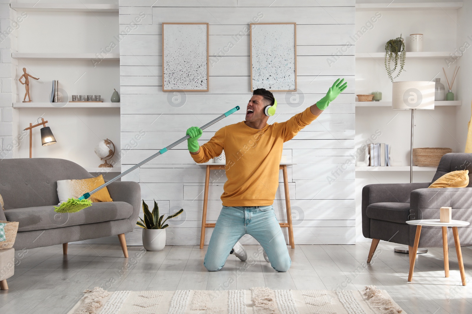 Photo of Man in headphones with mop singing while cleaning at home