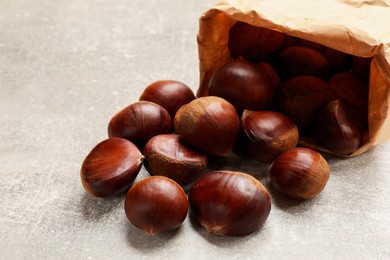 Paper bag with roasted edible sweet chestnuts on light grey table, closeup