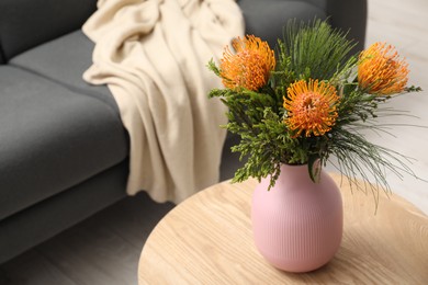 Beautiful flowers in vase on wooden coffee table near grey sofa indoors. Space for text