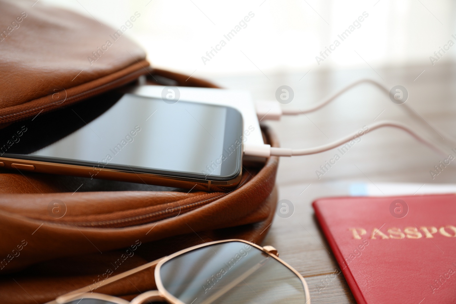 Photo of Charging mobile phone with power bank in backpack on wooden table, closeup