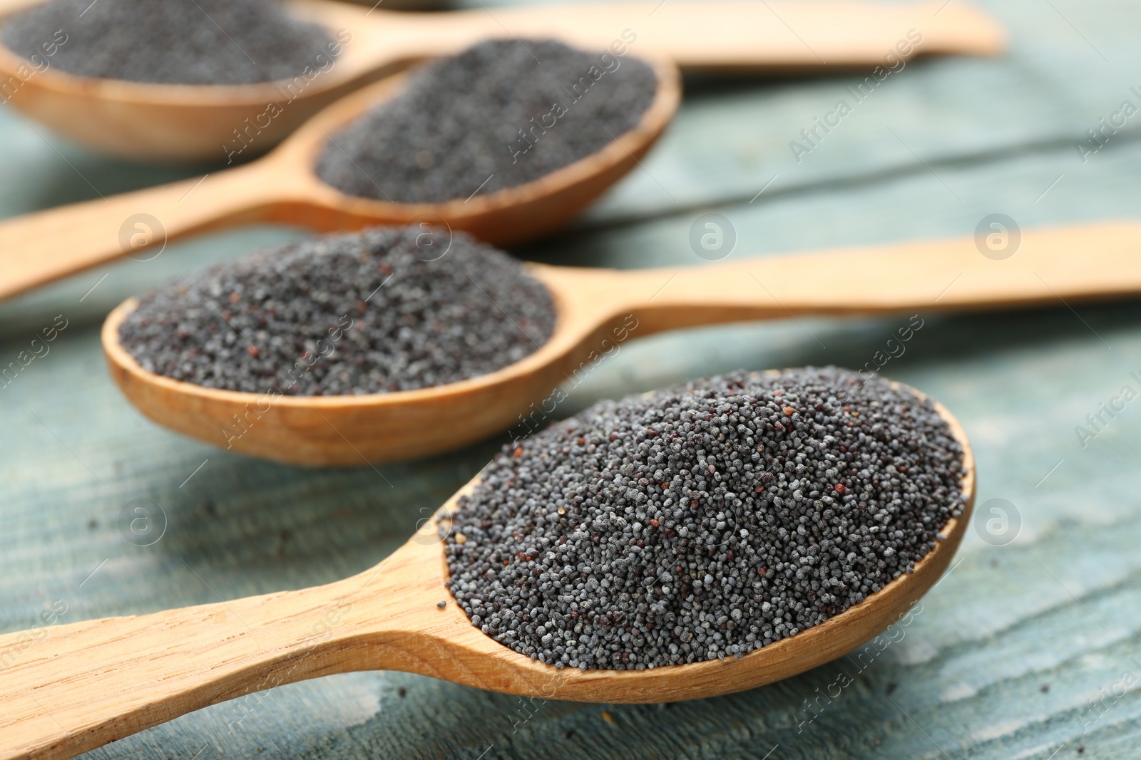 Photo of Poppy seeds in spoons on blue wooden table, closeup