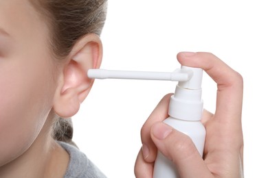 Photo of Mother spraying medication into daughter's ear on white background, closeup