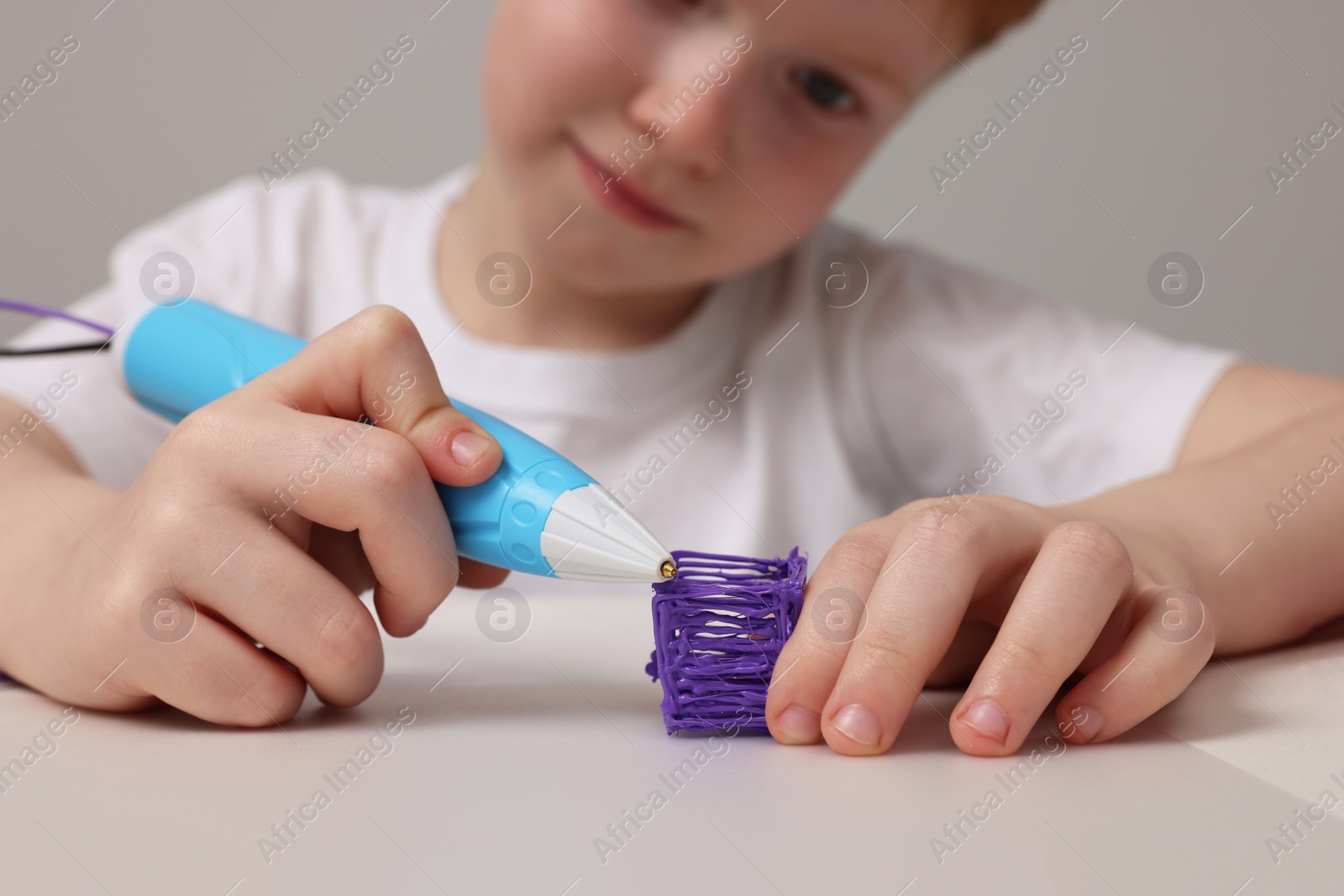 Photo of Boy drawing with stylish 3D pen at white table, selective focus
