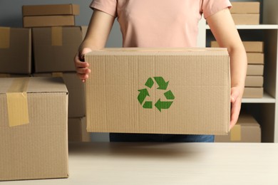 Image of Woman holding cardboard box with recycling sign stamp at white table indoors, closeup