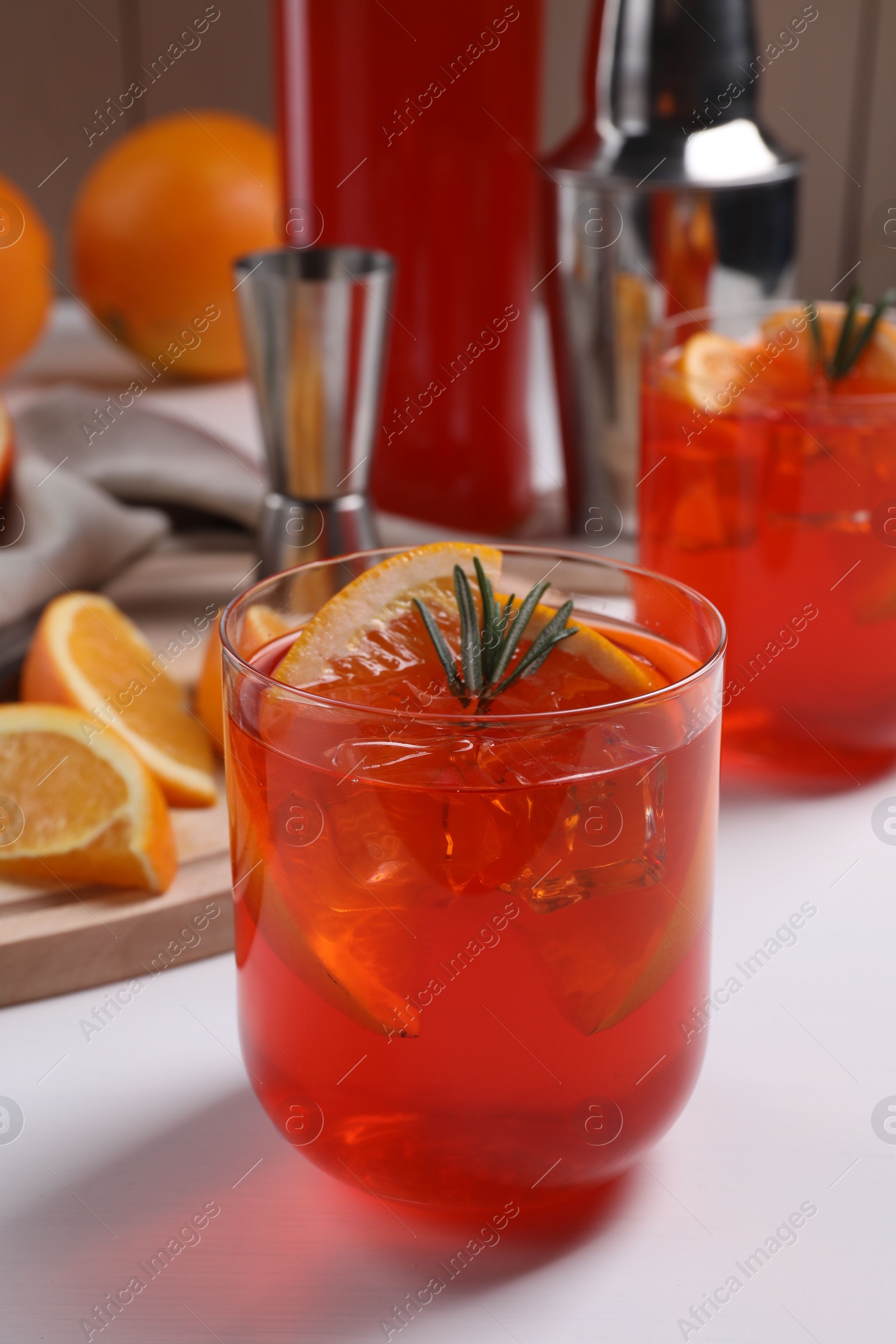 Photo of Aperol spritz cocktail, ice cubes, rosemary and orange slices in glass on white wooden table, closeup