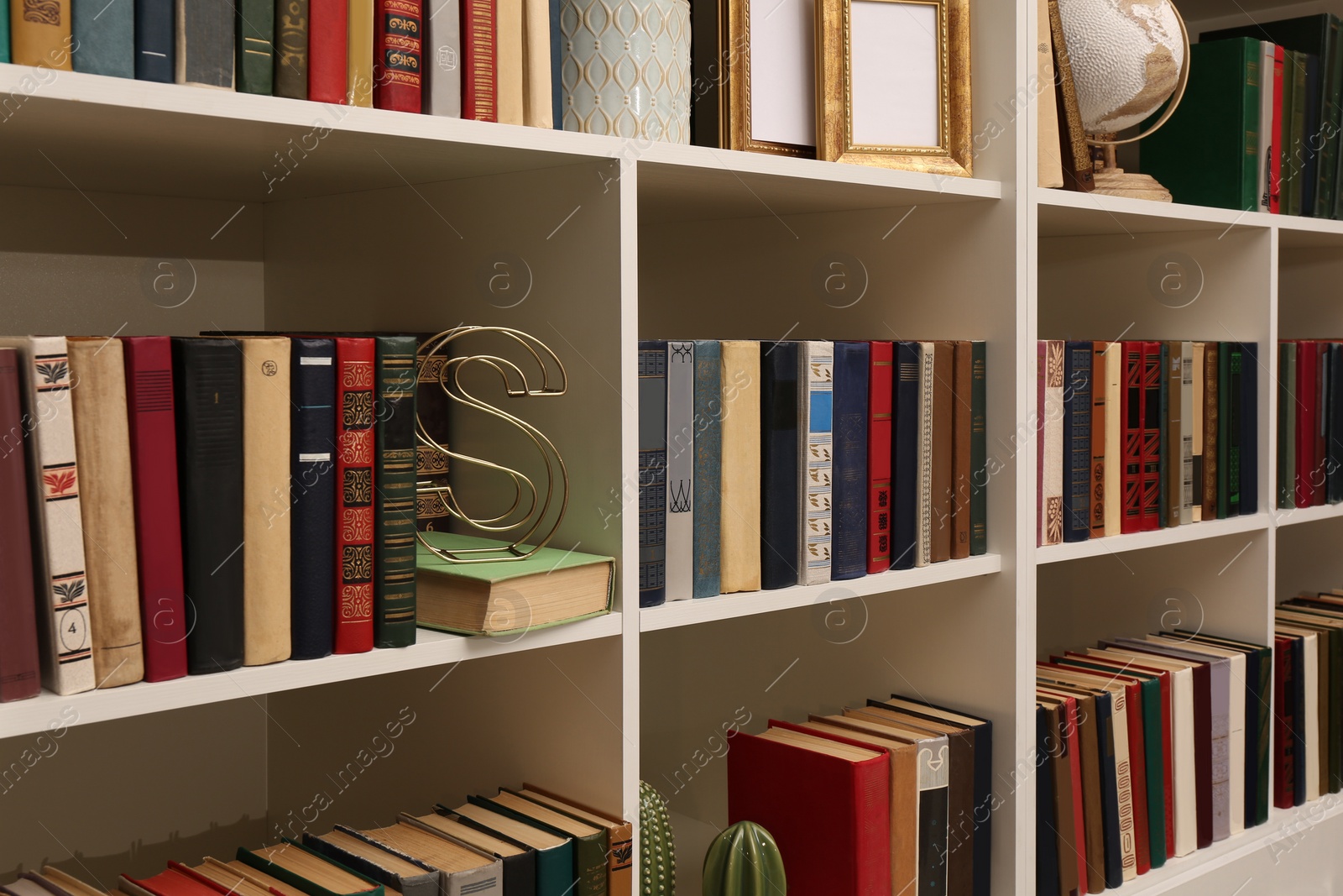 Photo of Collection of different books and decorative elements on shelves in home library