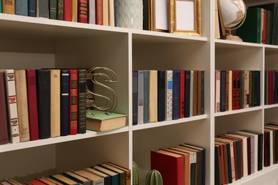 Photo of Collection of different books and decorative elements on shelves in home library