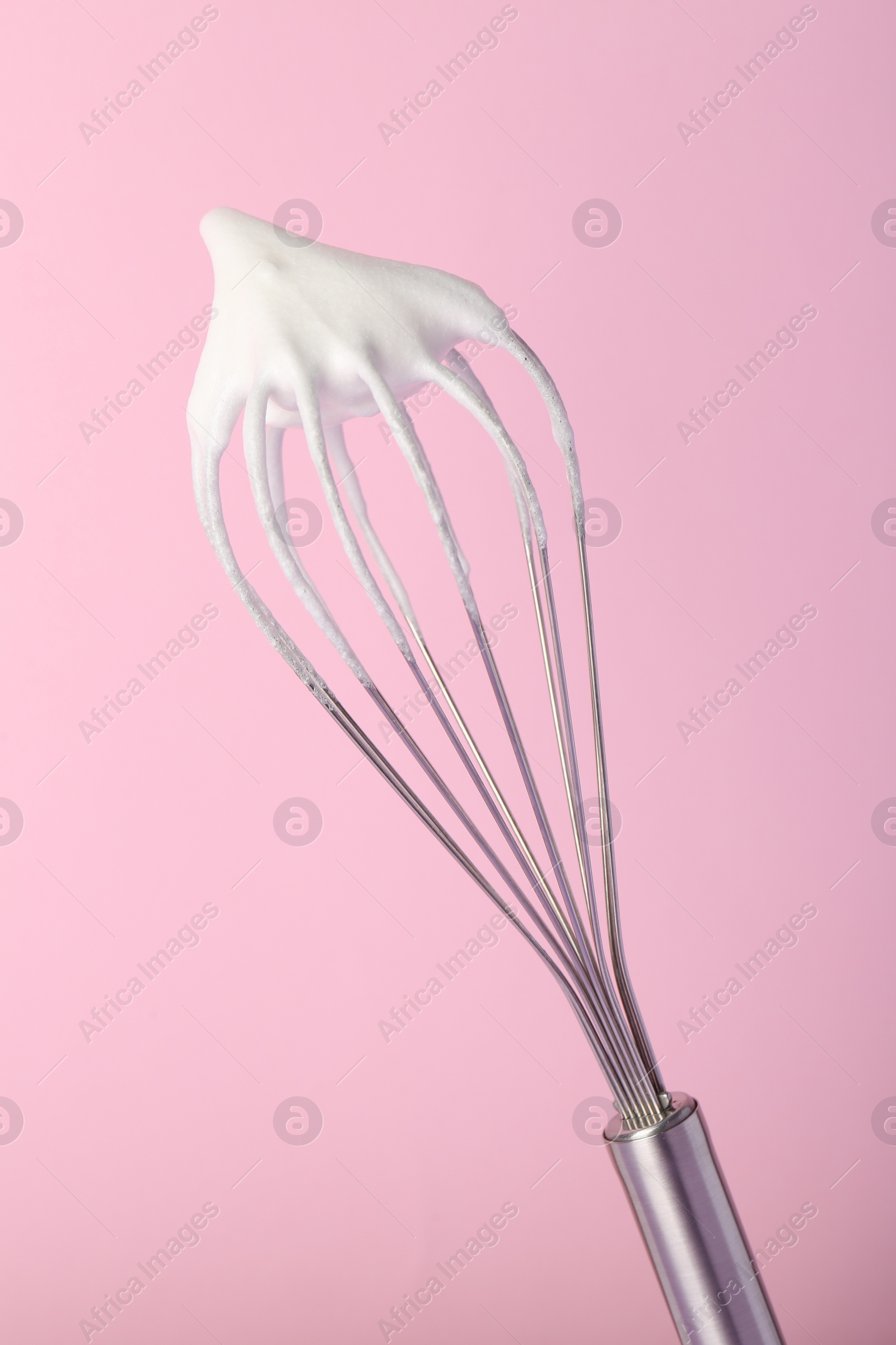 Photo of Whisk with whipped egg whites on pink background