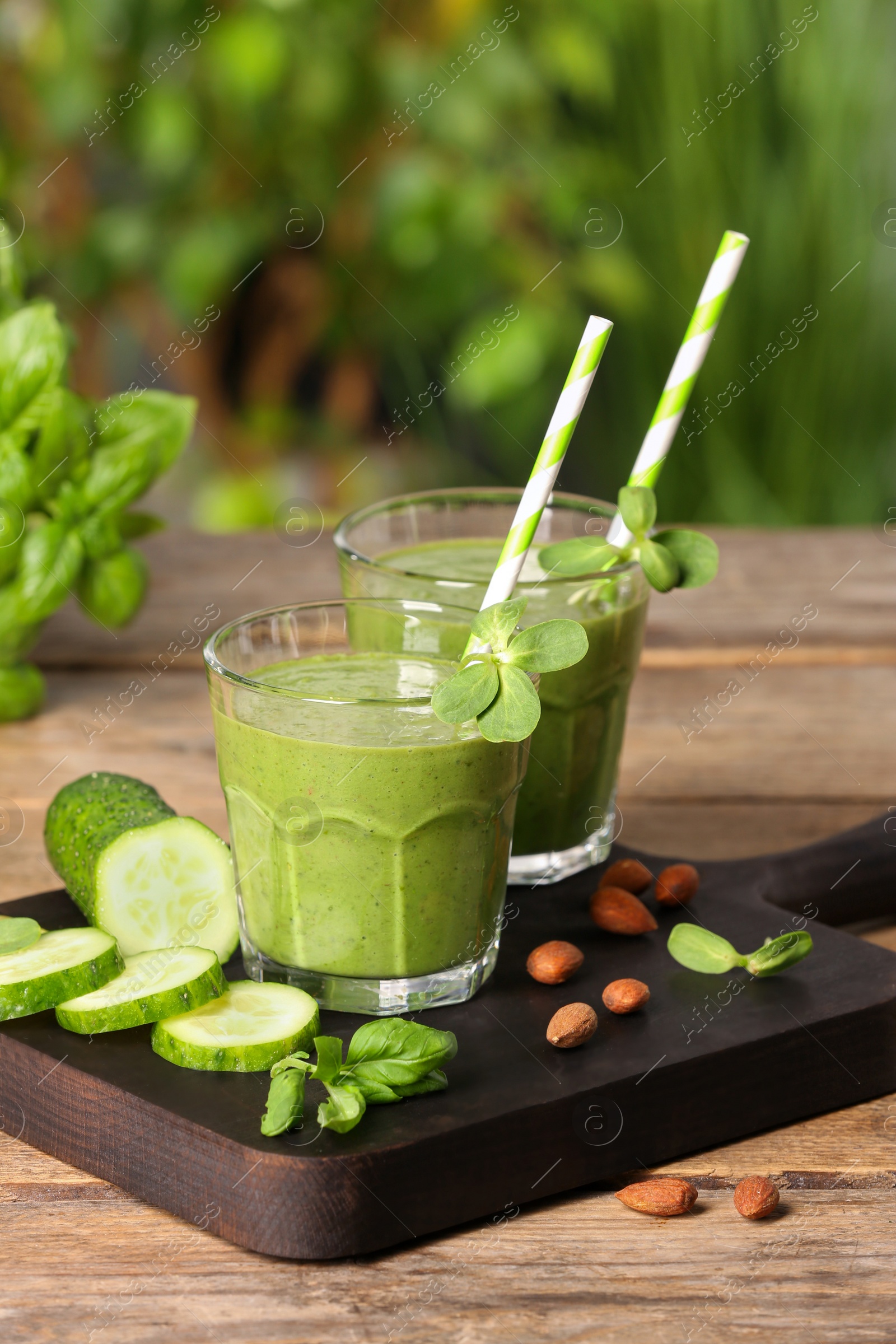 Photo of Glasses of fresh green smoothie and ingredients on wooden table outdoors, space for text