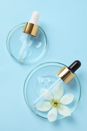 Photo of Petri dishes with samples of cosmetic oil, pipettes and beautiful flower on light blue background, flat lay