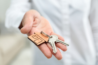 Photo of Real estate agent holding house keys with trinket, closeup