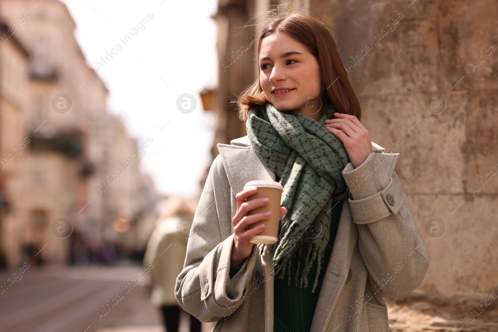 Photo of Beautiful woman in warm scarf with paper cup of coffee on city street, space for text