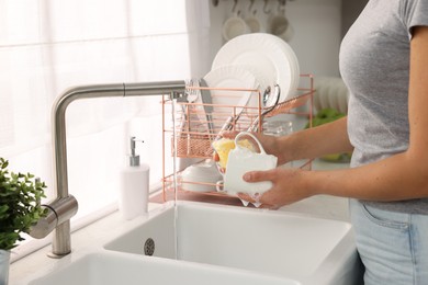 Photo of Woman washing cup at sink in kitchen, closeup