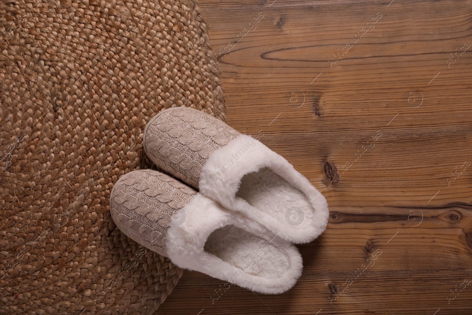 Photo of Pair of warm stylish slippers and wicker mat on wooden floor, flat lay. Space for text