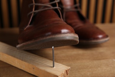 Photo of Metal nail in wooden plank and shoes on table, closeup