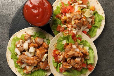Photo of Delicious tacos with vegetables, meat and ketchup on grey textured table, top view