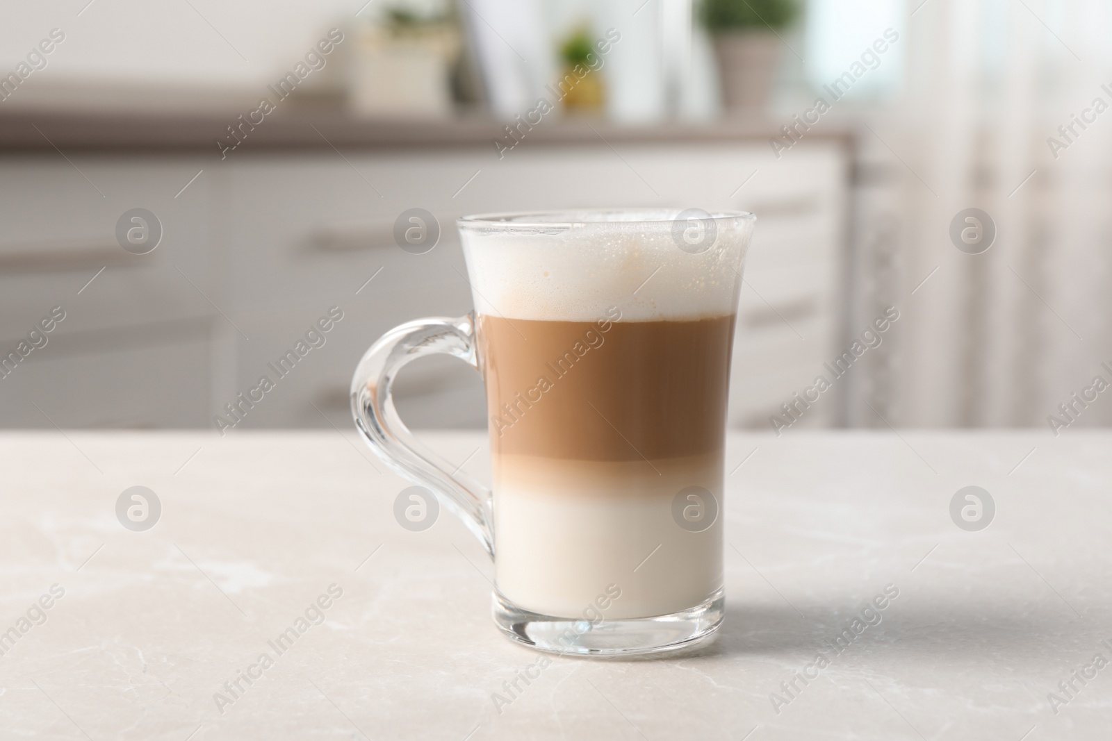 Photo of Glass cup of delicious layered coffee on light marble table indoors