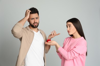 Young woman with engagement ring making marriage proposal to her boyfriend on light grey background