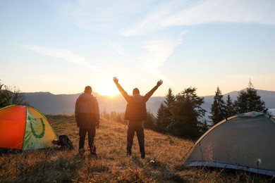 Photo of Men near camping tents in mountains at sunset, back view