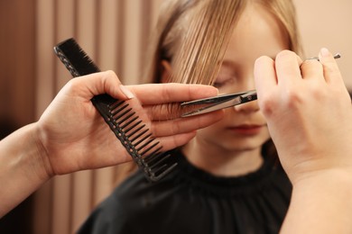 Photo of Professional hairdresser cutting girl's hair in beauty salon, closeup