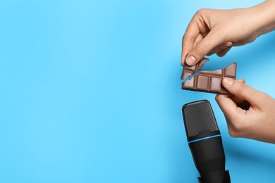 Photo of Woman making ASMR sounds with microphone and chocolate on light blue background, closeup. Space for text