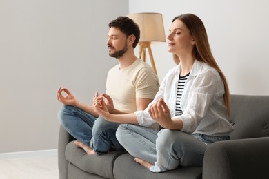 Photo of Couple meditating together on sofa at home. Harmony and zen
