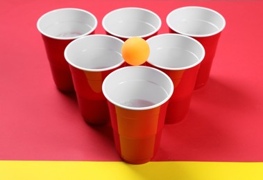 Photo of Plastic cups and ball for beer pong on color background