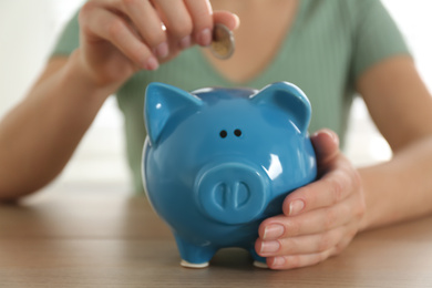 Photo of Woman putting money into piggy bank at wooden table indoors, closeup