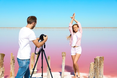 Professional photographer taking photo of woman near pink lake on sunny day