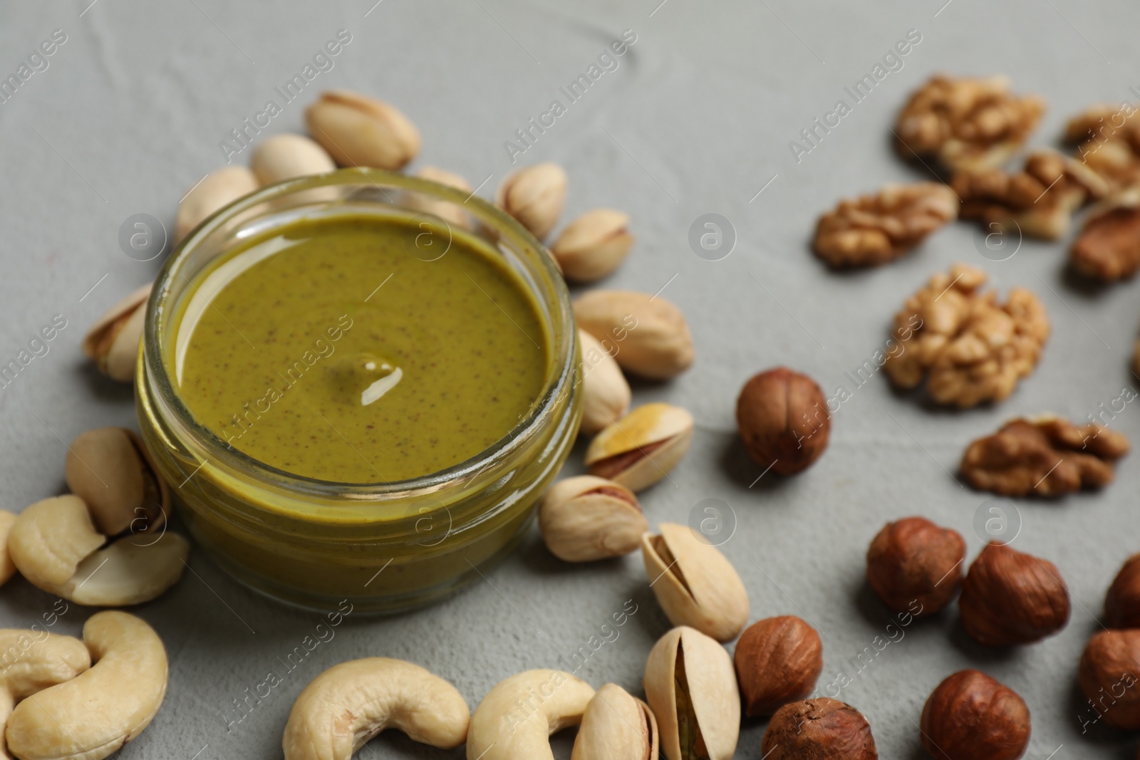 Photo of Delicious pistachio butter and different nuts on grey table, closeup