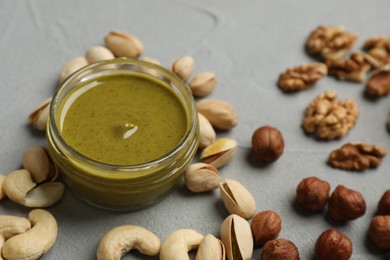 Photo of Delicious pistachio butter and different nuts on grey table, closeup